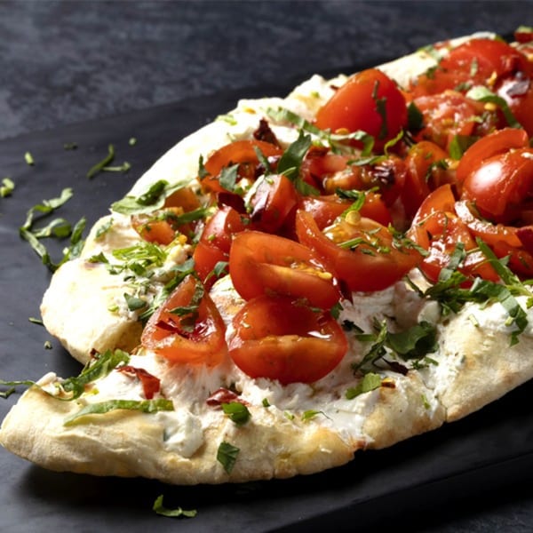 Rangeen Kitchen's naan bread topped with creamy cheese, fresh tomatoes, and green herbs.