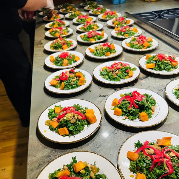 Multiple plates of kale salad with butternut squash, nuts, and pickled red onions, prepared for serving.