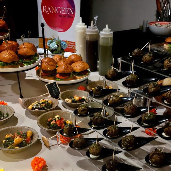 A buffet spread of Indian sliders, meatballs on spoons, and salads in bowls from Rangeen Kitchen.