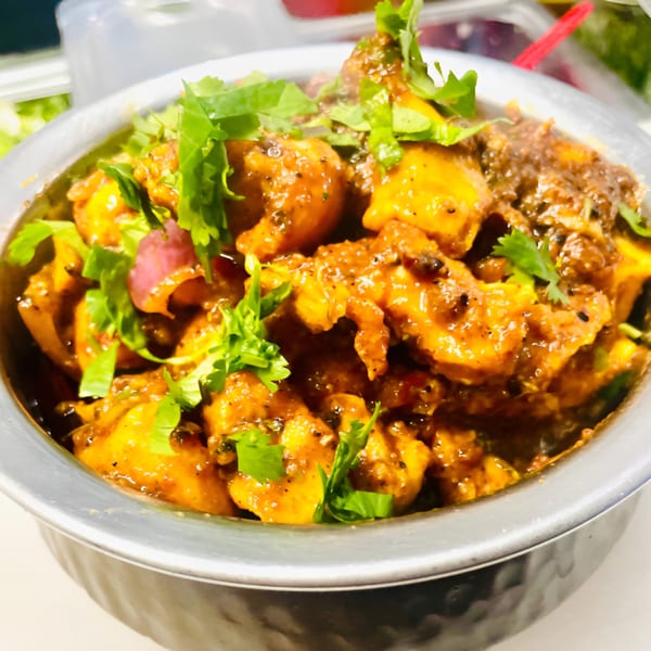 Rangeen Kitchen's Indian chicken curry, garnished with fresh cilantro and red onions in a metal bowl.