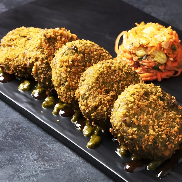 Five crispy Indian cutlets with green sauce and a side of shredded vegetables on a black plate.