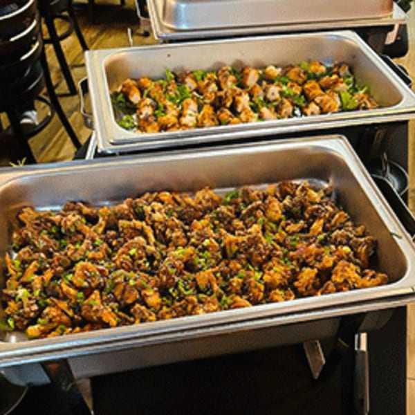 Two chafing dishes filled with Indian food, one with chicken and greens, the other with a dark, savory dish.