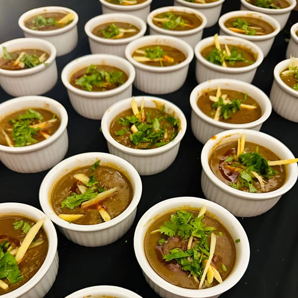 Multiple small white bowls of Indian dal, garnished with fresh cilantro and ginger, on a dark surface.
